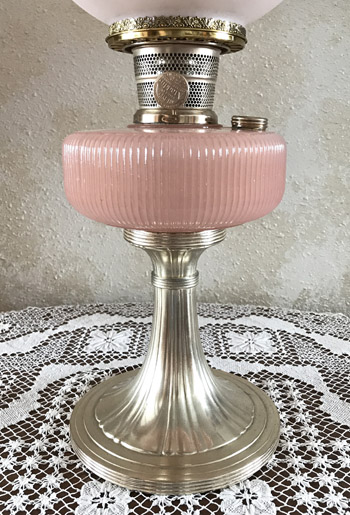 Vintage pink and silver oil lamp on a white lace tablecloth against a beige textured wall.
