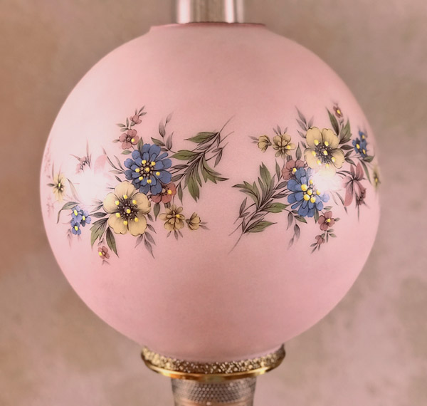 Pink round lamp shade decorated with blue and yellow flowers and green leaves.