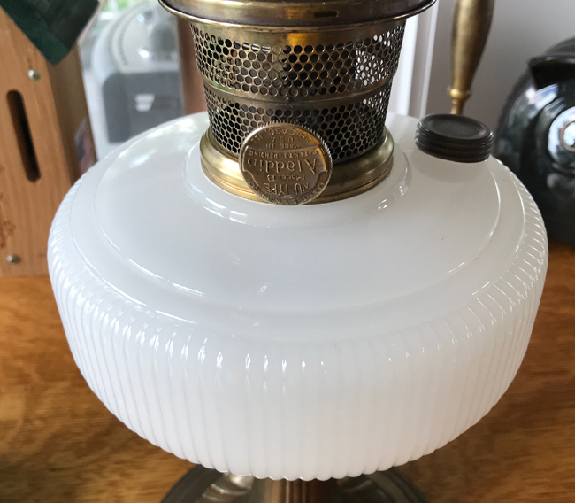 Close-up of a vintage white glass oil lamp with a brass wick holder and adjustment knob.