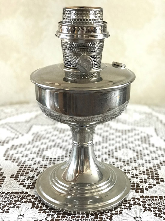 Vintage polished metal oil lamp with a perforated burner on a lace tablecloth.