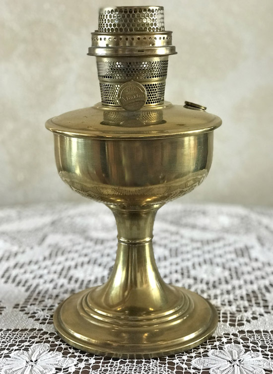 Vintage brass oil lamp with a pedestal base on a lace tablecloth.