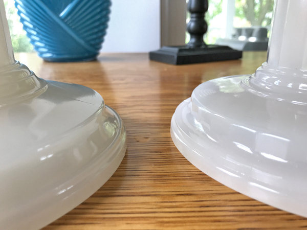 Close-up of two white circular lamp bases on a wooden surface with blurred blue vase and window background.