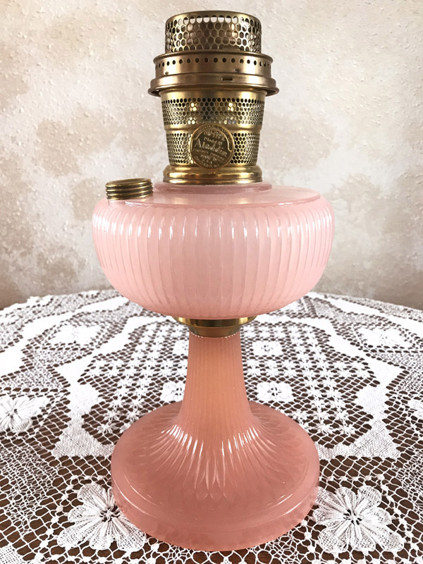 Vintage pink glass oil lamp with brass burner on a white lace tablecloth.