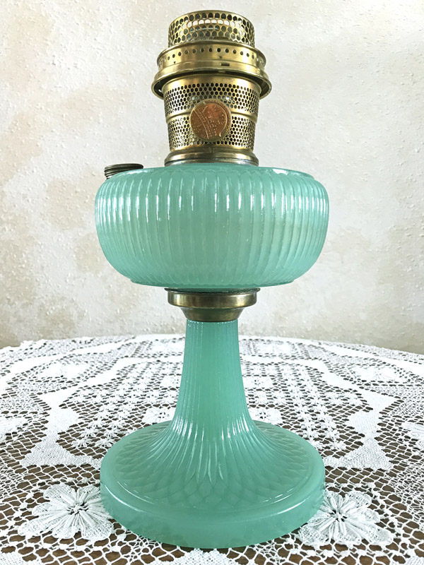 Vintage green glass oil lamp with brass burner on white lace tablecloth.
