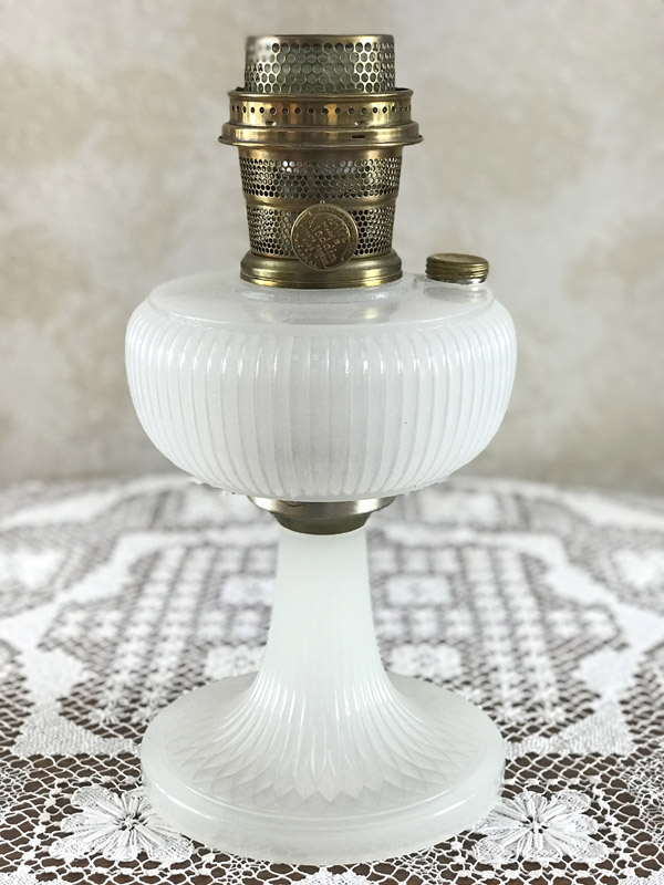 Vintage white glass oil lamp with brass burner on lace tablecloth.