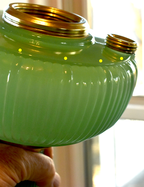 Hand holding green ribbed glass jar with brass threaded openings near a window.