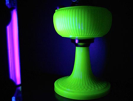 Glowing green vintage glass lamp base illuminated under ultraviolet light against a dark background.