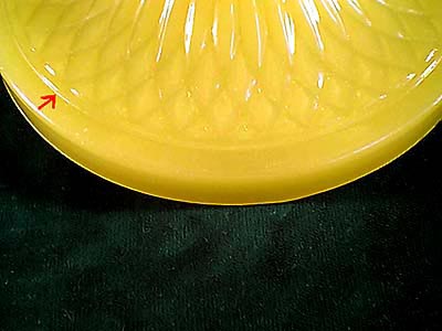 Close-up of a yellow glass plate with textured patterns and a red arrow marking a small chip on the edge.
