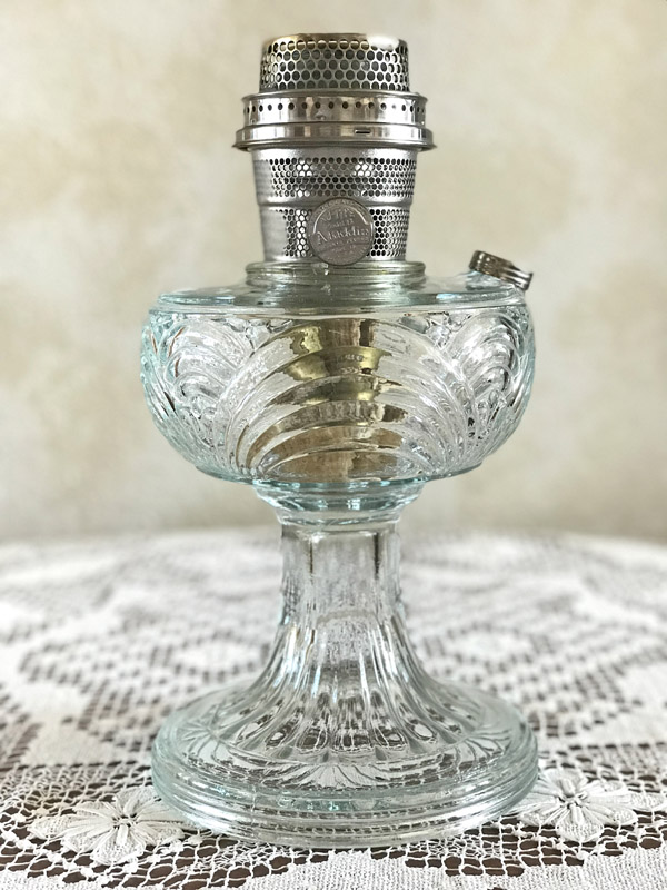 Vintage clear glass oil lamp with ornate design and metal wick holder on a lace table cover.