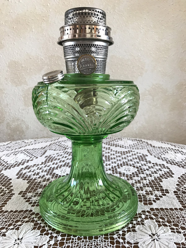 Green glass vintage oil lamp with intricate patterns on a lace tablecloth.