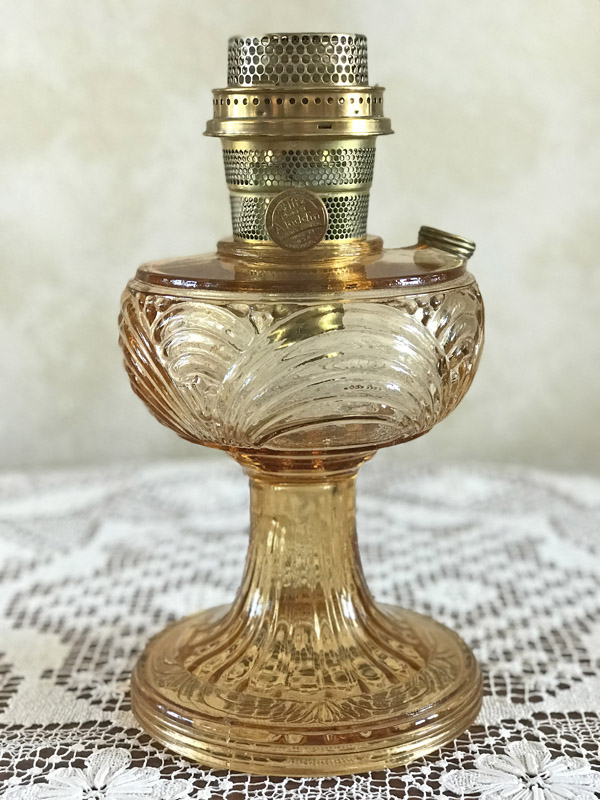 Antique amber glass oil lamp with ornate base and brass burner on lace tablecloth.