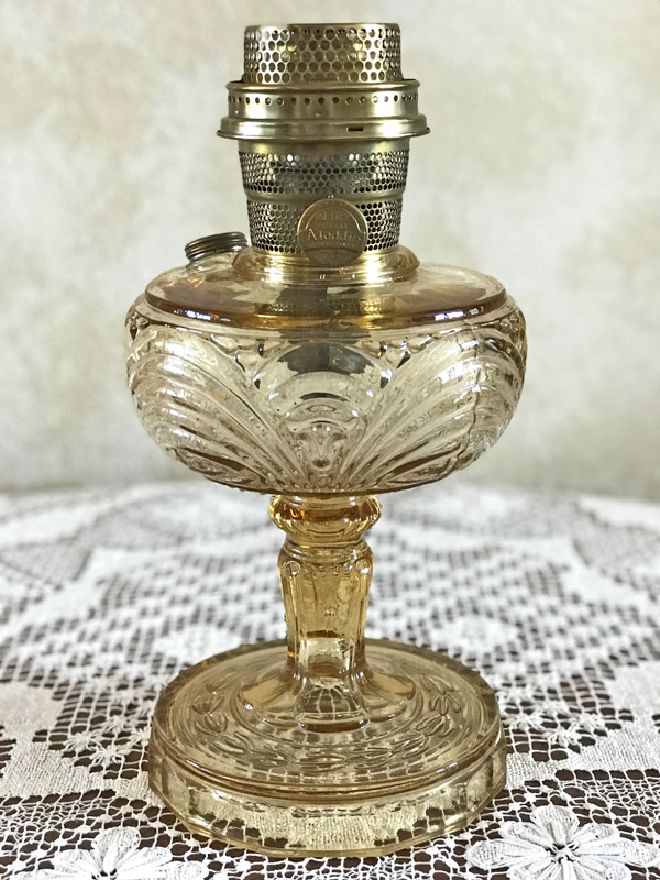 Amber glass oil lamp with intricate filigree pattern on a lace tablecloth.