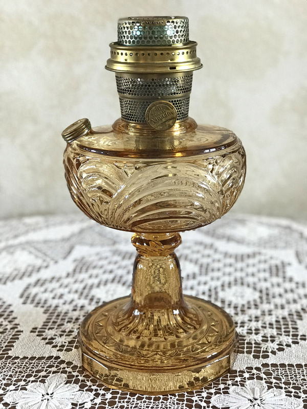 Amber-colored vintage glass oil lamp with ornate pedestal base on lace tablecloth.