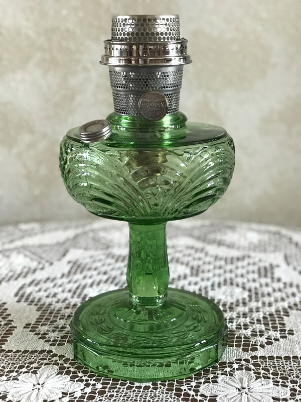 Vintage green glass oil lamp with metal burner on a lace tablecloth.