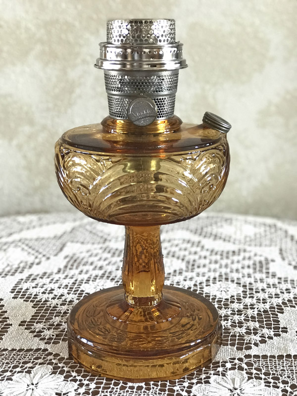 Amber-colored glass oil lamp with a decorative pattern on a lace tablecloth.