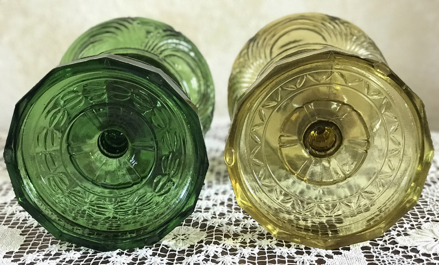 Bottom view of two vintage pressed glass cups, one green and one yellow, on a lace surface.