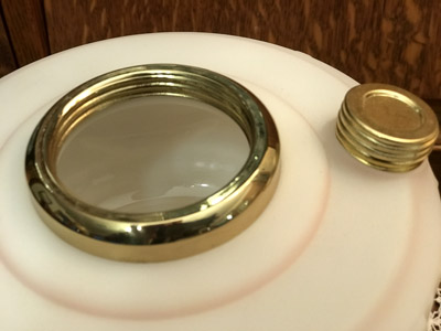Close-up of a round white container with a large brass-trimmed opening and a smaller brass cap beside it.
