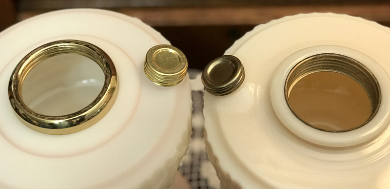 Close-up of two white porcelain lampshade holders with metal threaded openings and matching metal caps.