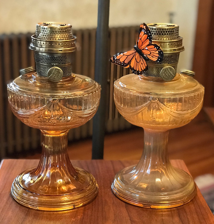 Two amber glass oil lamps on a wooden surface with one decorated by an orange butterfly.