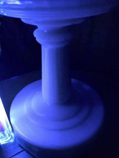 Close-up of a blue-lit white marble pedestal with a fluted column and round base.