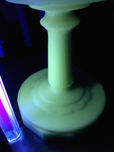Close-up of a glowing green pedestal or candle holder lit by a nearby purple light tube in darkness.