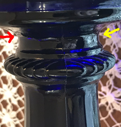 Close-up of a cobalt blue glass stem with a visible crack and background lace fabric.