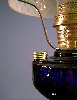 Close-up of a vintage brass and blue glass oil lamp burner with wick holder and curved handle.
