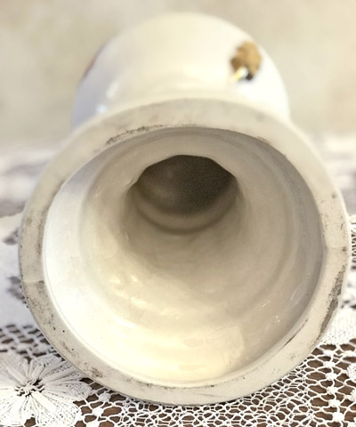 Close-up inside view of a white vintage ceramic vase lying on a lace tablecloth.