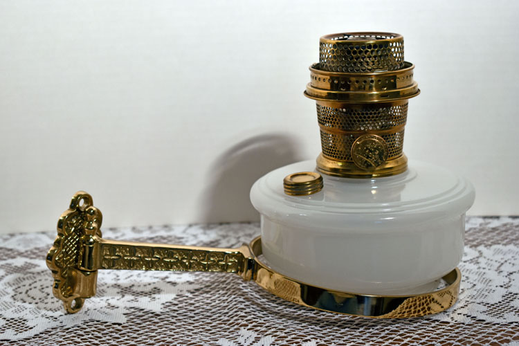 Vintage brass and white glass kerosene lamp with ornate wall mount on lace cloth.