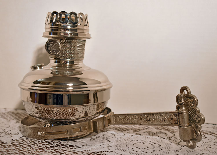 Shiny antique metal oil lamp with detailed handle placed on lace fabric surface.