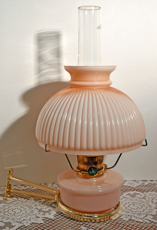 Vintage pink glass oil lamp with ribbed shade and clear chimney on lace tablecloth.