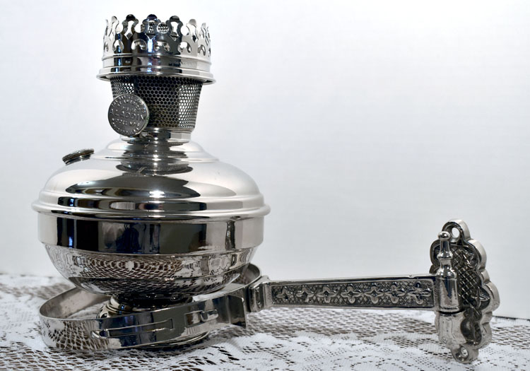 Shiny silver vintage oil lamp with ornate handle resting on lace fabric.