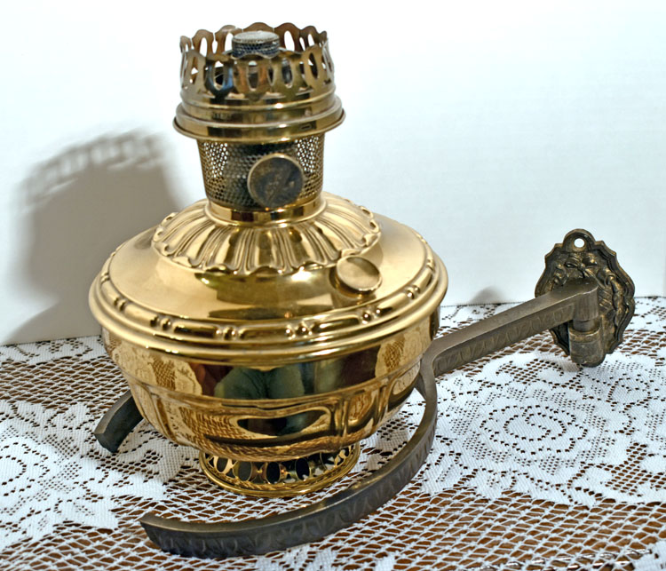 Vintage brass oil lamp with curved metal bracket on a white lace cloth.