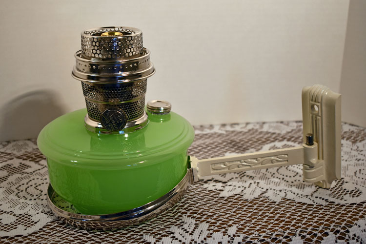 Green vintage kerosene heater with metal wick adjustment on lace-covered surface.