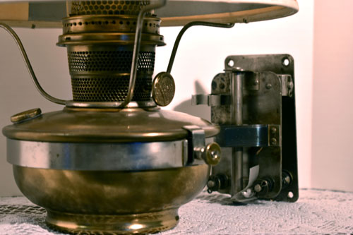 Close-up of a vintage brass lamp base and metal wall bracket on a lace-covered surface.