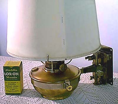 Vintage brass Aladdin oil lamp with white shade and green box of Lok-On mantles on lace surface.