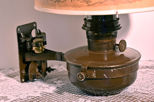 Close-up of a vintage brown oil lamp on a lacy tablecloth with a partially visible lampshade.