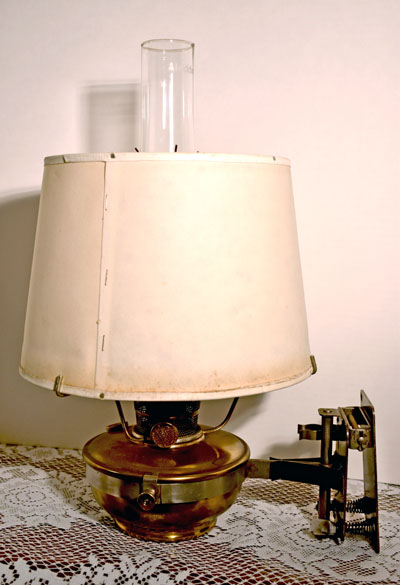 Vintage brass oil lamp with a white fabric shade and clear glass chimney on lace tablecloth.