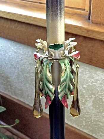 Close-up of decorative metal candle holder with hanging glass prisms in front of a window.