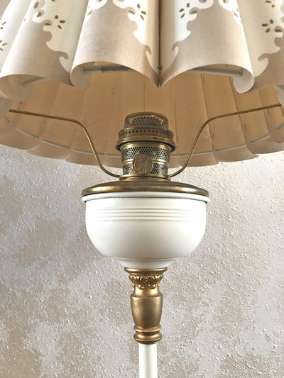 Close-up of a vintage lamp with a beige pattern lampshade and decorative gold and white base.