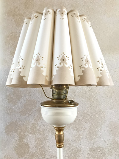 Vintage lamp with brown and white scalloped shade featuring cut-out patterns on textured wall.