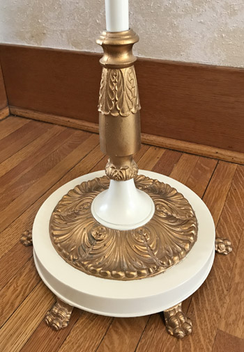 Ornate gold and white candlestick holder with leaf patterns on a wooden floor.