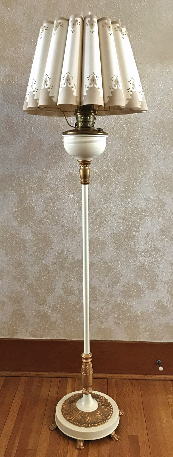 Tall vintage floor lamp with cream and gold ornate base and a pleated beige lampshade with decorative cutouts.