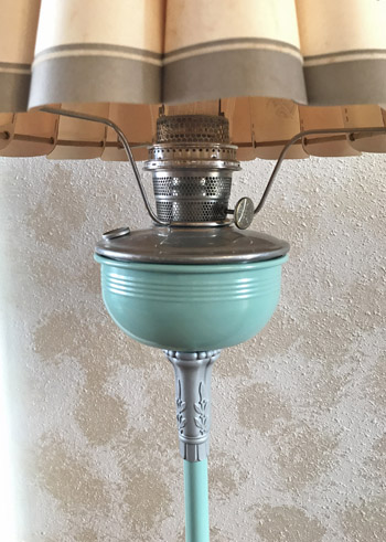 Close-up of a vintage floor lamp with a teal glass base and beige fabric shade.
