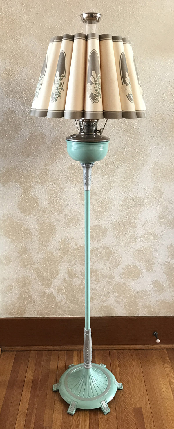Vintage floor lamp with pleated cream shade and turquoise ornate base standing on wood floor.