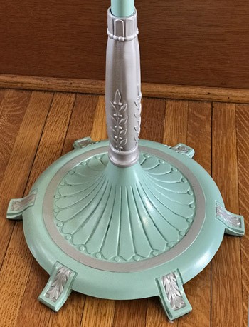 Decorative mint green lamp base with silver leaf accents on a wooden floor.