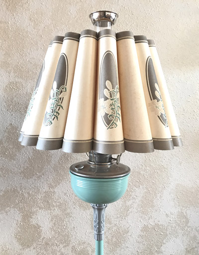 Vintage floor lamp with pleated beige shades and teal ceramic base against a textured wall.