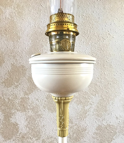 Close-up of a vintage brass and white oil lamp with glass chimney against a textured wall.