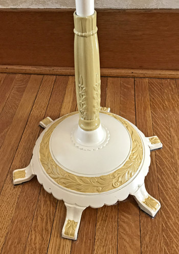 Decorative lamp base with white and gold floral designs on a wooden floor.