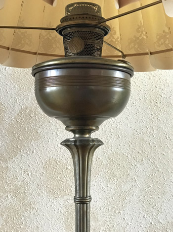 Close-up of a vintage metal oil lamp with a glass shade against a textured wall.